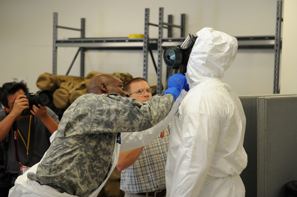 Maj. John Dills (left), the 36th Engineer Brigade chief of current operations, helps zip and close the protective suit of Sgt. 1st Class Venrick James, also from the 36th Eng. Bde., during training inside the Medical Skills Training Center at Fort Hood, Texas. Soldiers trained to work in buddy teams to put on and take off their protective equipment, a measure aimed at minimizing the chance of contamination. Photo: Staff Sgt. Daniel Wallace, III Corps Public Affairs
